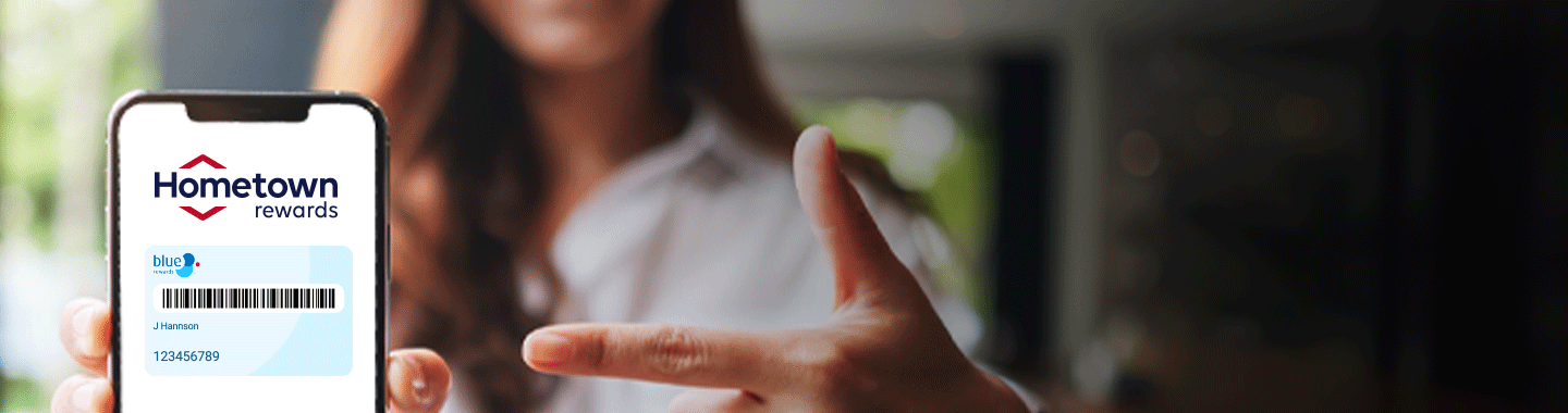 A women holding a phone with Hometown rewards app opened and she is pointing towards the phone with her thumbs up and index finger at the phone